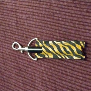 A  Silver key ring  with black and gold metallic prints that holds a lip gloss.